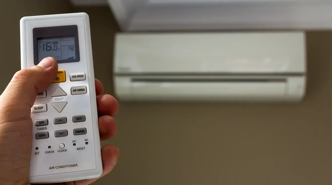 A hand adjusts the air conditioning temperature on a remote control.