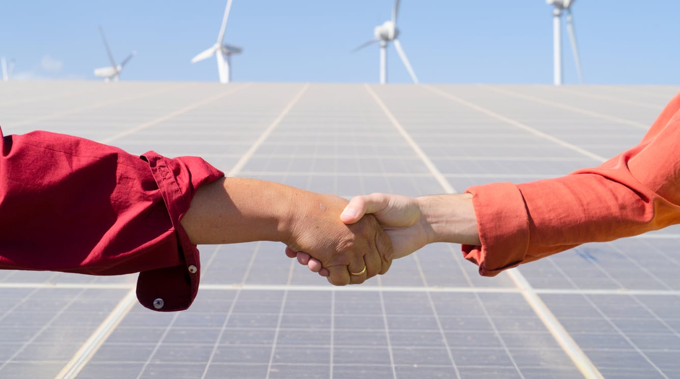 Handshake in front of solar panels and wind turbines.